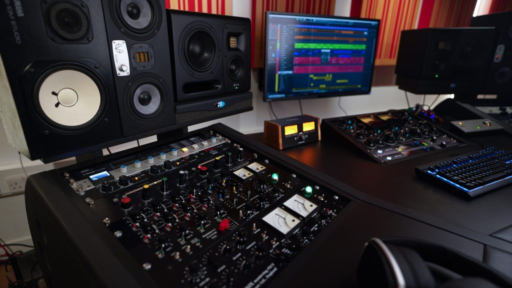 Side view of Doctor Mix studio showing multiple speakers, analogue gear, and computer with audio program